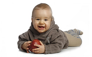 baby wearing brown hoodie while holding red apple
