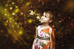 girl in white, orange, and green floral sleeveless dress infront of green plants during daytime