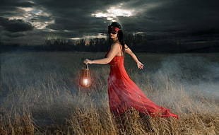 woman wearing red dress while holding candle lantern during nighttime
