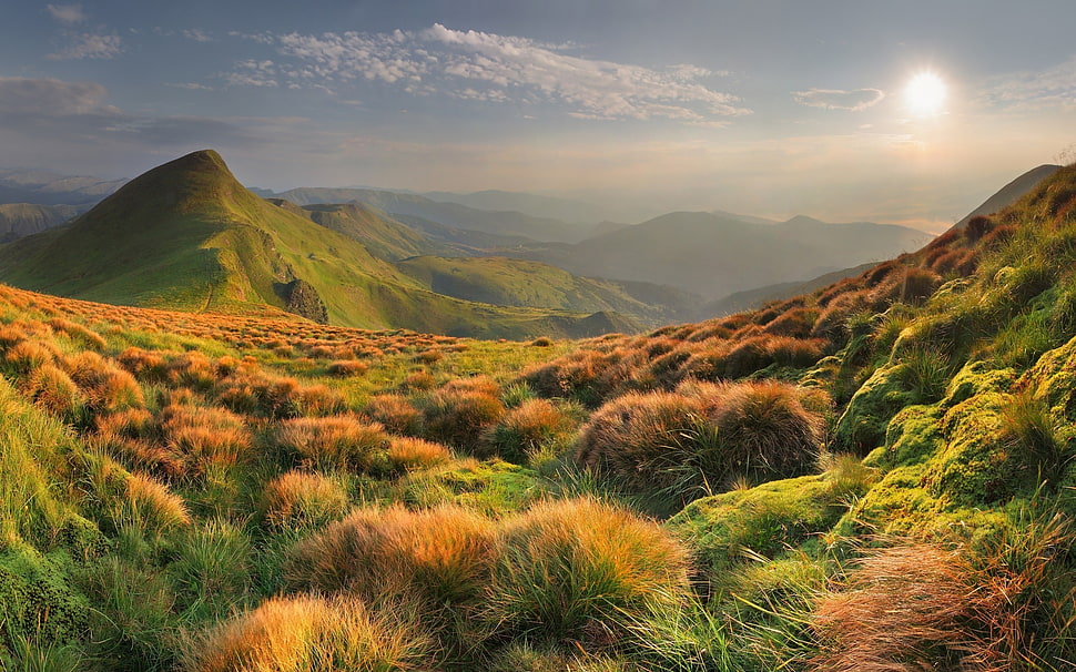 green grassy field overlooking mountains under cloudy sky at daytime HD wallpaper