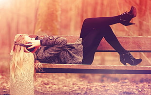 woman in grey jacket lying on brown wooden bench wearing black headphones