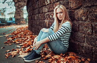 woman sitting on floor with leaves while leaning on wall