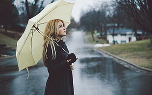 woman in black coat under white umbrella standing on road at daytime