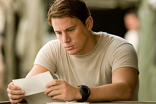 man in beige crew-neck shirt reading note on white paper