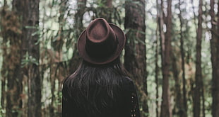 woman with brown fedora hat facing the woods at daytime