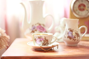 auto focus photography of white floral teacup on white ceramic saucer with gold necklace placed in it HD wallpaper