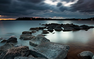 photo of body of water with rock formation under cloudy skies