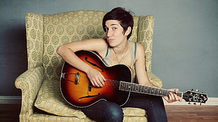 woman in brown tank top holding acoustic guitar