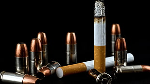 two cigarettes and several bullet cases on black surface