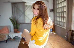 woman wearing yellow long-sleeved top sitting on brown wooden table taking picture