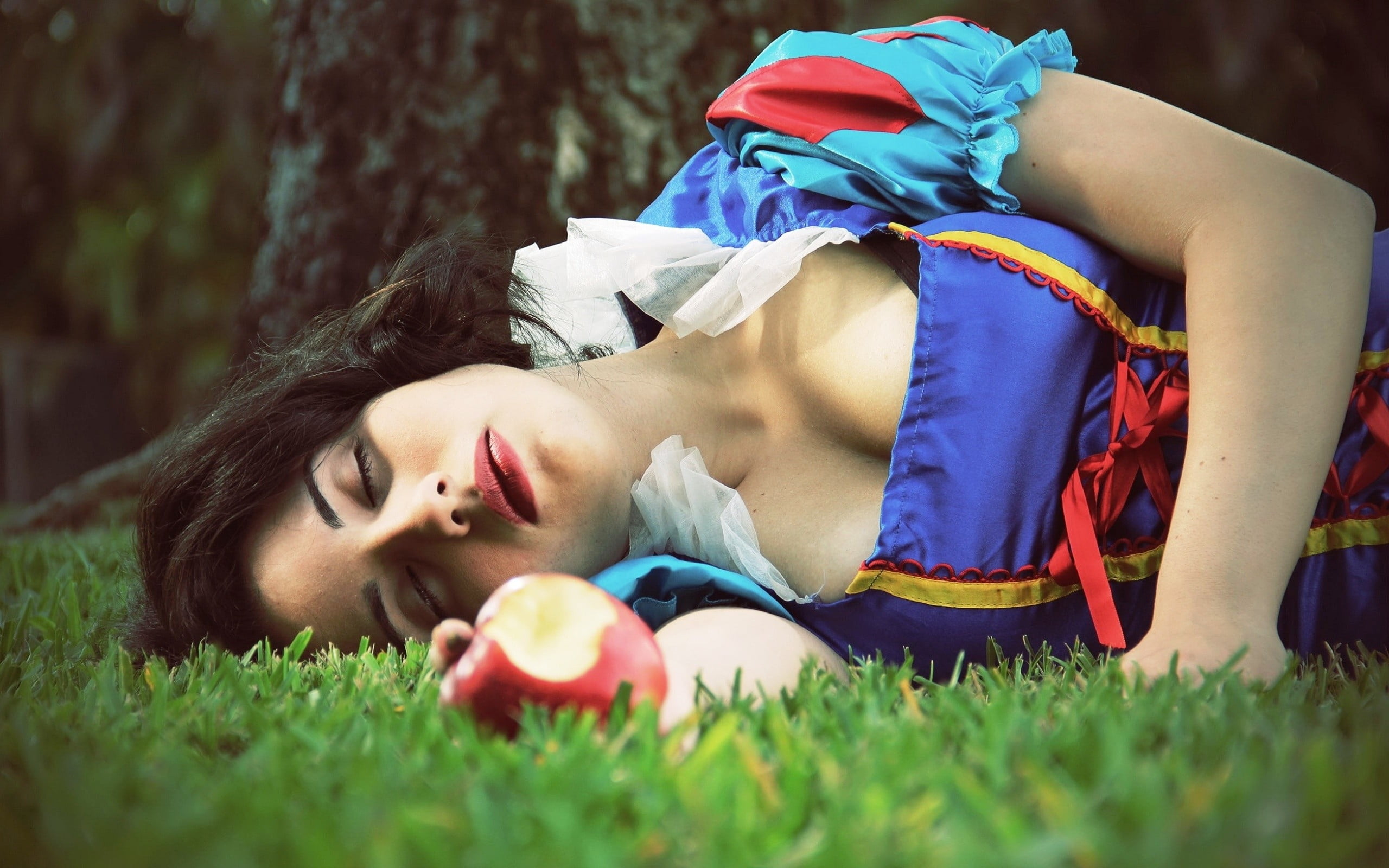woman in blue and red Snow White costume lying on green open field holding ...