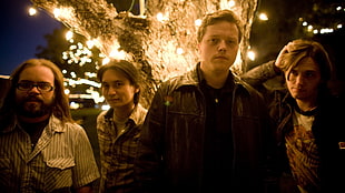 four men stands beside brown tree with string lights turned on