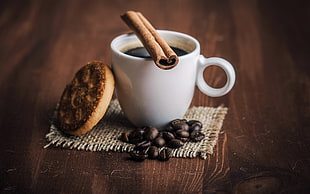 white ceramic mug, coffee beans, and brown cookie on brown wooden surface