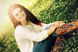 woman wearing white cardigan and blue denim jeans while sitting at the green grassfield