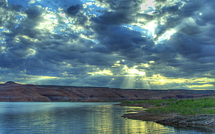 body of water surrounded by mountains with sun rays