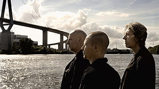 three man standing near body of water during day time