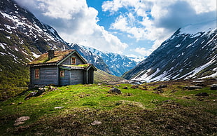 brown wooden house near mountain under cloudy sky