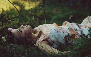 closeup photo of woman in white floral dress lying on green grass