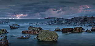 stones on shore with lightning on sky HD wallpaper