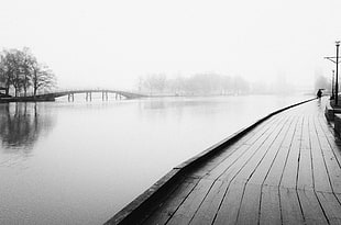 greyscale photo of person walking beside calm body of water HD wallpaper