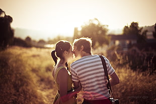 man in white and gray kissing woman in green dress during sunrise