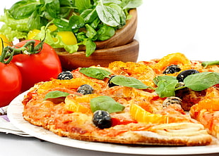 thin crust pizza with black olives and green vegetables beside two orange tomatoes