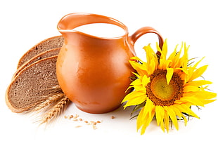 brown ceramic pitcher with milk beside sunflowe and three slices of bread