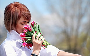 woman wearing white collared shirt snipping bouquet of pink tulips during daytime