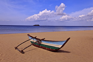 blue, white, green, and red wooden boat on brown beach