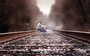 woman wearing sports shirt and denim jeans while sitting down at the center of a railroad