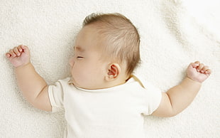baby in white top lying on white surface
