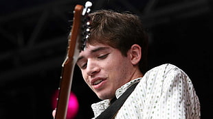 man wearing white dress shirt while playing a brown and black electric guitar