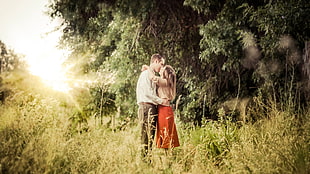 photography of man and woman kissing while standing on grass while facing sunlight