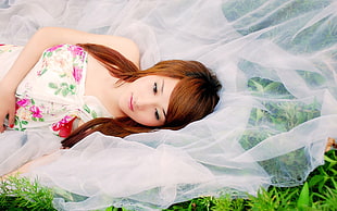 woman wearing white, green, and pink floral tube dress laying on white textile during day time