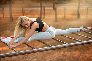 woman wearing black sports bra doing split on gray metal bars during daytime