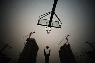 worm's eye view of man shooting basketball on hoop surrounded by buildings with cranes in vigenette filter HD wallpaper