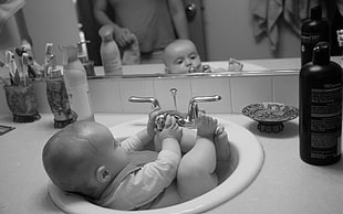 grayscale photograph of baby on ceramic sink