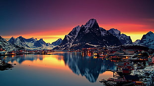 clear calm body of water in front ice covered mountains under orange and blue sky