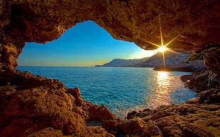 cave beside body of water during sunrise
