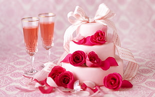 3-tier fondant cake covered by pink rose flowers beside champagne flute glasses filled with brown liquid