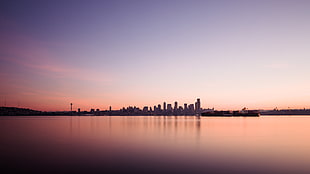 city buildings beside body of water under clear sky during sunset