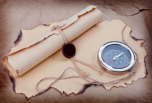 round silver-colored framed compass on brown printed paper