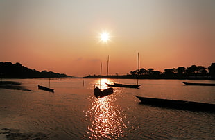silhouette of boats on body of water during sunset