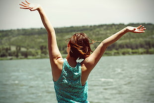 woman in tank top raising her hands in front of body of water during daytime