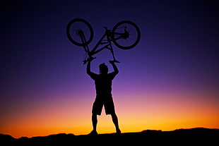 silhouette of man carrying mountain bike during sunset