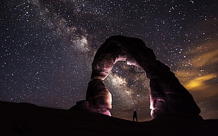 person standing in rock arch under starry skies