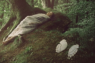 woman wrapped with white textile lying on green moss beside brown tree
