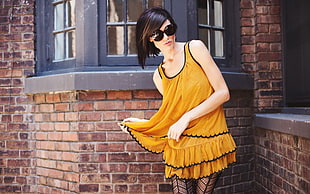 woman in yellow and black sleeveless dress beside concrete bricks wall