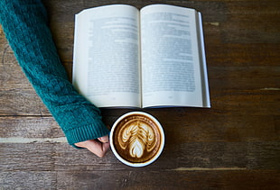 round white ceramic mug with cappuccino in it beside book HD wallpaper