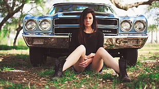 woman sitting on ground in front of blue Chevrolet Camaro